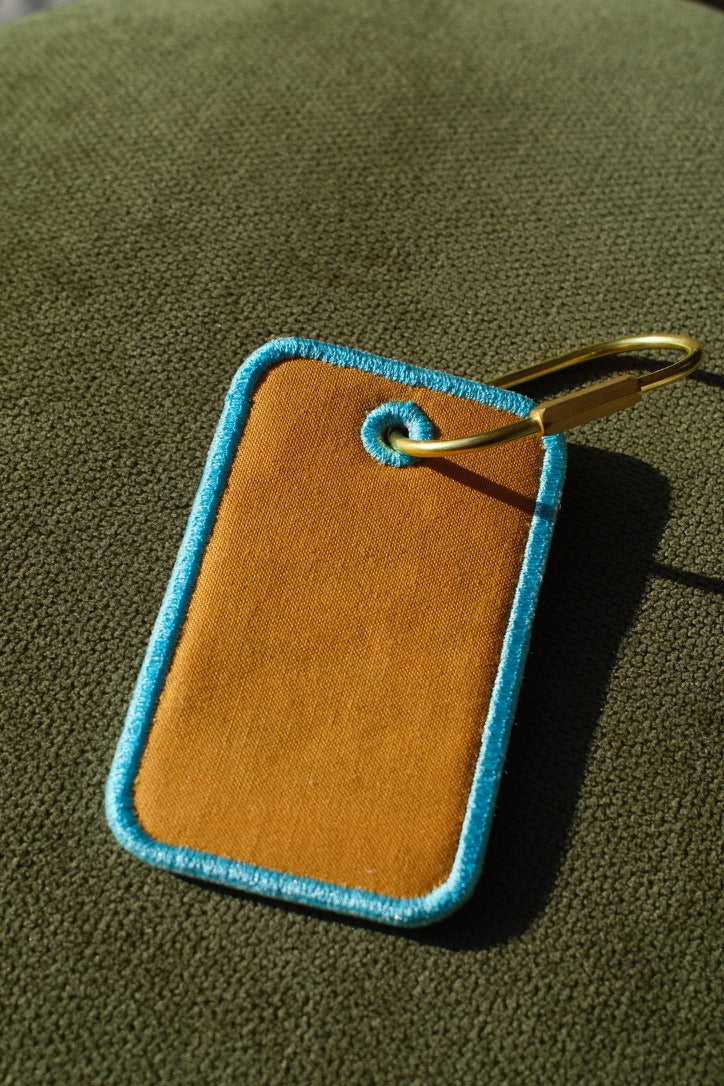 Orange Puerto Rico stamp embroidered luggage tag

Puerto Rican bag charm with gold-tone carabiner

Aqua embroidery detail on Puerto Rico travel tag

Puerto Rico luggage tag attached to a suitcase

Front and back of embroidered Puerto Rico bag tag