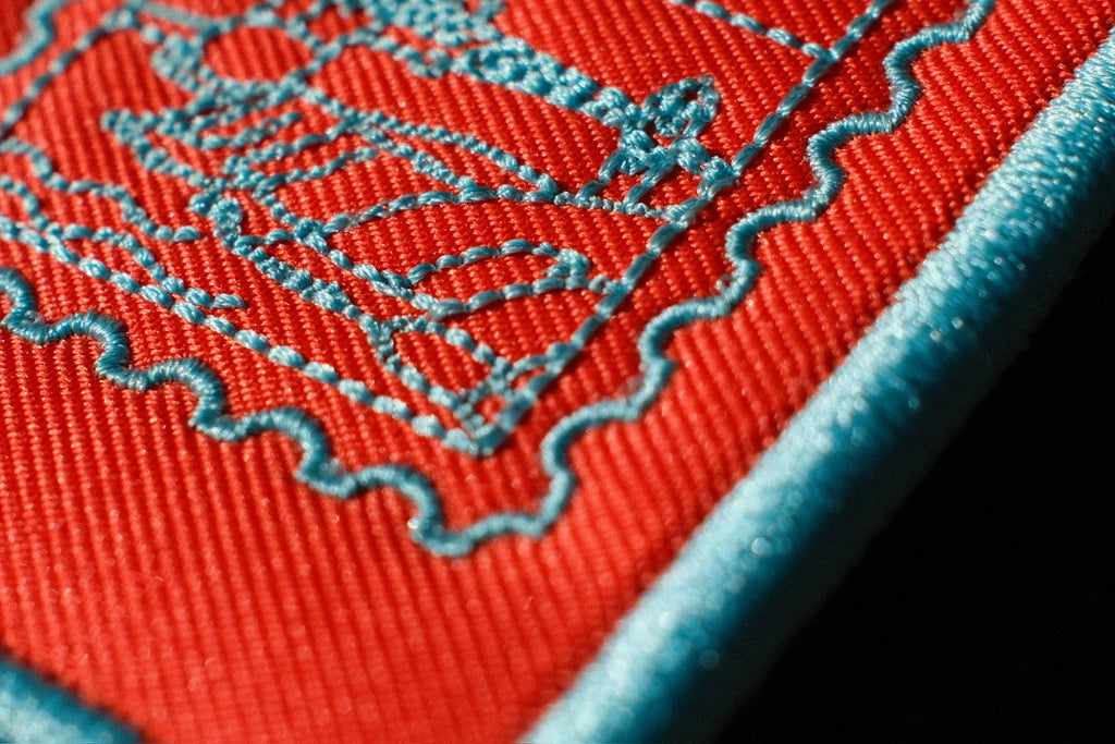 Orange Puerto Rico stamp embroidered luggage tag

Puerto Rican bag charm with gold-tone carabiner

Aqua embroidery detail on Puerto Rico travel tag

Puerto Rico luggage tag attached to a suitcase

Front and back of embroidered Puerto Rico bag tag